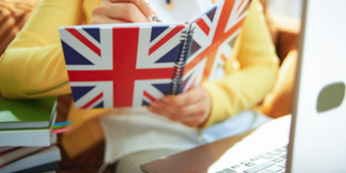 Close up photo of a woman in front of a laptop writing in a notebook with the UK flag