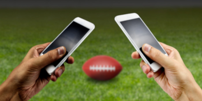 Close up photo of the hand of a black man and a white man, each holding a smartphone, symbolizing sports betting