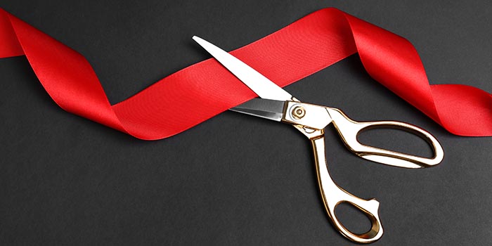 A pair of scissors cuts a red ribbon