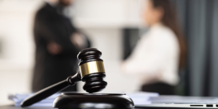 A close up photo of a judge's hammer and mallet with two blurry people in background, symbolizing lawsuit