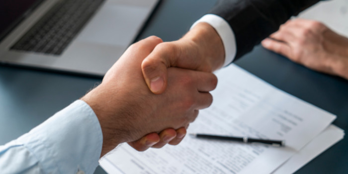 Two businessmen shake hands on top of signed documents, close up photo